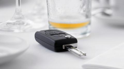 A stock image of a black car key on a table covered with a white cloth with an empty beer glass near it