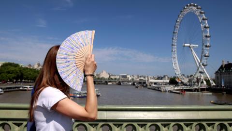 Woman fans herself on a hot sunny day in London with the London Eye in the background
