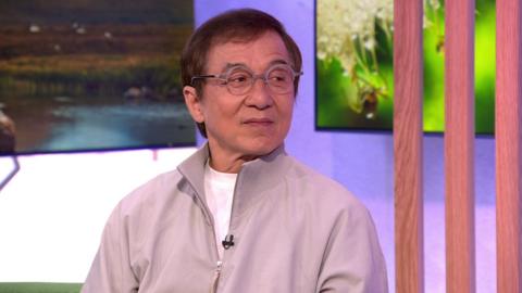 Jackie Chan wears round glasses and a beige tracksuit