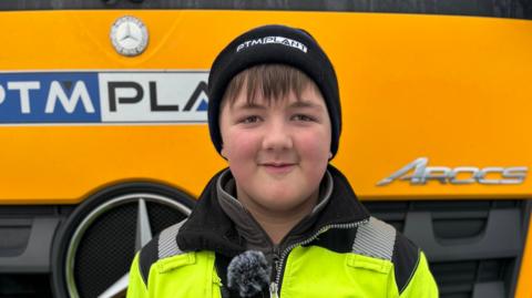 Jamie Monaghan, a teenage boy, is wearing a black woolly hat and a yellow high-vis jacket.