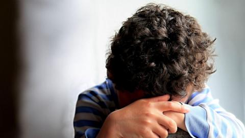 A boy sitting down with his hands covering his face, as if in despair. 