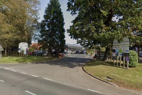 The entrance to the Garden Centre, with large trees framing the driveway into it. The signs either side it read 'Bell Plantation' 