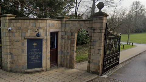 The gates to the Church of Scientology with a small building in pale stone with two doors - one with a cross on it