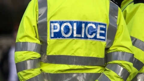 The back of a police officer, who is wearing a hi-vis coat with "police" on the back of it.