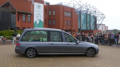 Fans applaud as the funeral cortege of John Clark passes Celtic Park