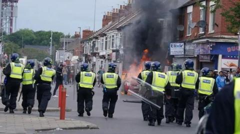 Riot police in Middlesbrough during the summer riots. A property is on fire.