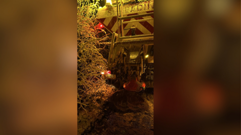 A gritter lorry with it's red hazard light on, on the side of a snowy road.