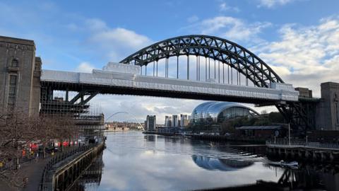 The Tyne Bridge. Large white sheets cover much of the bridge where repair work is being carried out. Scaffolding can be seen underneath the bridge by the concrete towers.