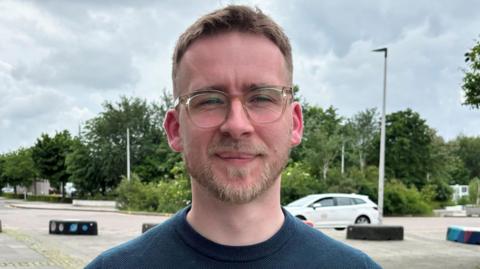 A picture of Fraser Stewart outside while wearing a blue sweatshirt and glasses. 