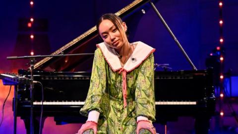 Griff in a green dress sitting at a piano