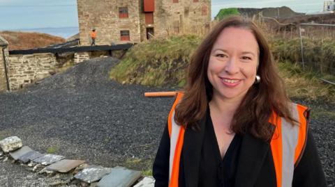 Bryony Robinson is wearing a Hi-Viz jacket and is standing in front of the historic John O' Groats mill.