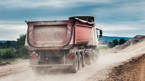 An industrial dumper truck driving on a dusty highway construction site.