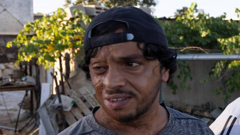 Odeh Hathaleen is pictured with a beard and curly hair, wearing a backwards baseball cap and a t-shirt, outside