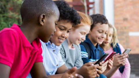 A line of five children looking at their phones
