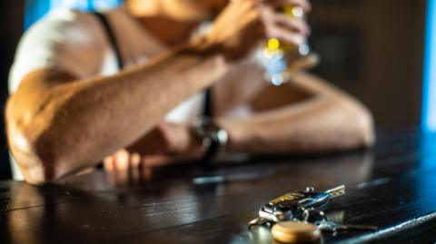 Car keys in focus with a blurred background of a man sat down holding a pint