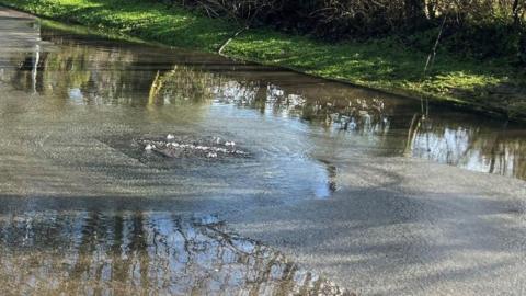 A drain in a road is overflowing and the road is flooded.