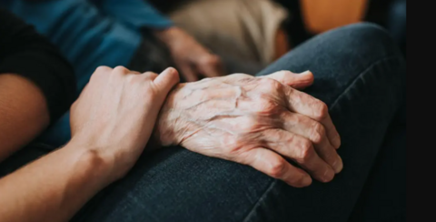 An older hand is held by a younger hand. You can't see the faces of either person