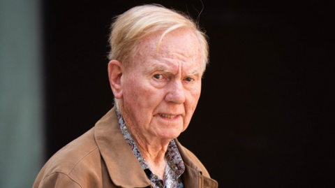 A man in a brown jacket and a patterned shirt