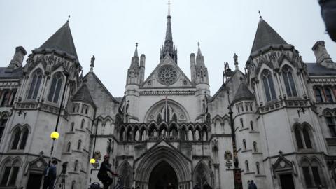 People gathering around the Royal Courts of Justice, a grand, gothic building with pointed roofs and arches, on a grey day
