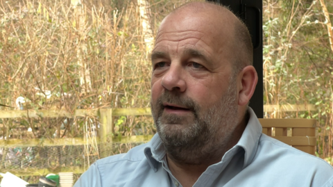 A picture of Andy Smith sitting down inside, behind a garden.