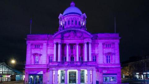 The photo shows Hull City Hall lit up in purple at night. 