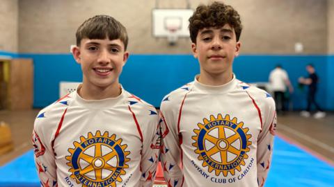 Liam on the left and Finn on the right in white gymnastics tops with the Rotary International logo on the front.