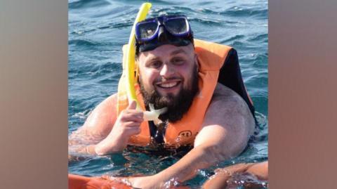 Mohammed Hasan snorkling in water. He is smiling on the photo and wears a pair of snorkling glasses on his head.