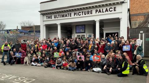 A crowd of people outside Oxford's Ultimate Picture Palace cheering and holding signs.