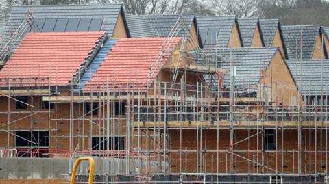 A number of homes in a row at an under-construction housing development. Scaffolding has been set up in the foreground.
