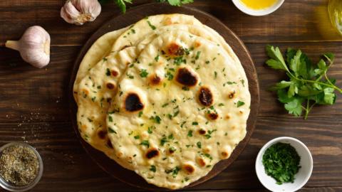 Top view of garlic butter naan and some of the ingredients laid out on a wooden table