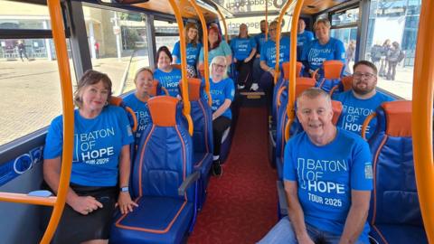 A group of men and women sitting on a bus. They are all wearing blue T-shirts. 