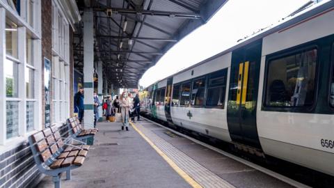 Epsom station platform. There is a masked woman walking down the plat form where a Southern train is waiting. 