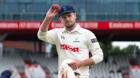 Mason Crance holds a cricket ball to acknowledge fans at the Old Trafford cricket ground