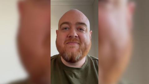 Artificial intelligence education expert Dan Fitzpatrick wearing a green top on a plain background. He has a beard and has his mouth closed