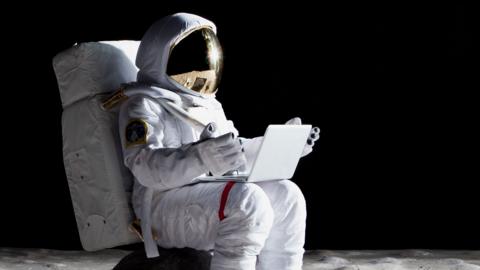 An astronaut sat on the moon, holding a laptop