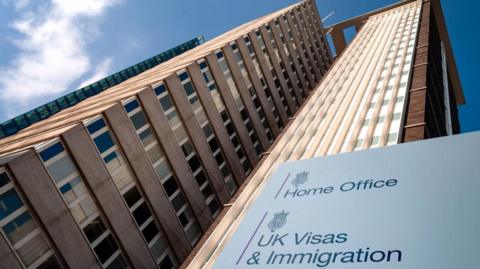 A tall rise building with a sign in front of it saying 'Home Office' and 'UK Visas & Immigration'