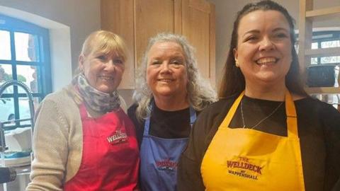Kal Wood, who runs the cafe, is pictured in the centre of this picture wearing a blue apron. Her daughter Ellie wears a yellow apron and stands on the right and Ms Wood's "good friend and volunteer" is Ellen in a red apron on the left. The three women are standing in the newly-reopened cafe.