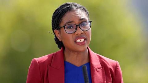 Kemi Badenoch wearing a red jacket and blue top