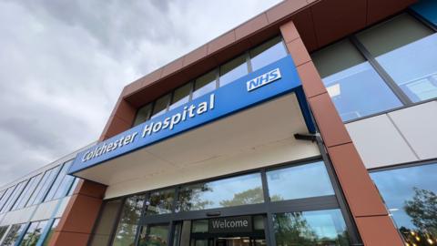 A glass sliding door at the entrance to Colchester Hospital with the word "welcome" above it