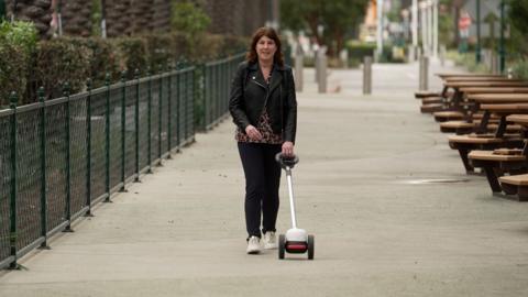 Emma Tracey uses a Glide - a device with two wheels and a long handle - on a walkway