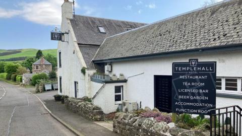 An old white Borders pub building with a slate roof and sign for tea room and accommodation