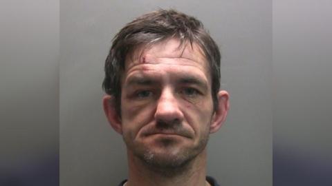 A mug shot of an unshaven man with facial injuries 