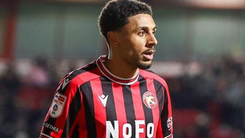 Brandon Comley looking to the right of frame in a red and black striped Walsall shirt