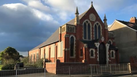 A red-bricked church. Some windows along its side appear to be boarded up.