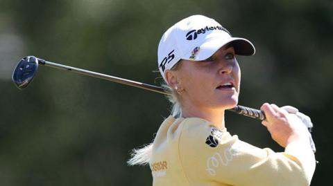Charley Hull, wearing a yellow top and white cap, with her golf club over her back left shoulder in her follow through