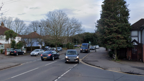 A suburban road with trees and grey cars. 