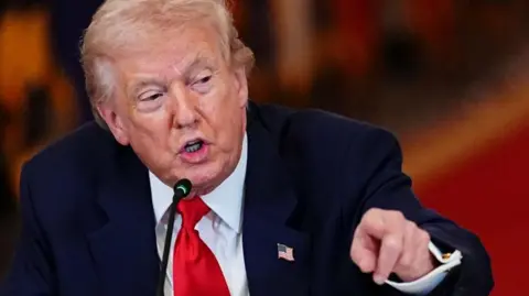 Donald Trump wearing a dark suit pointing at the camera