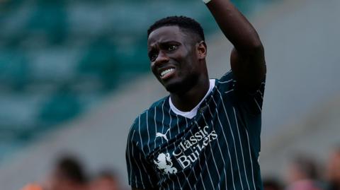 Michael Baidoo raises his arm to the bench after feeling his hamstring injury