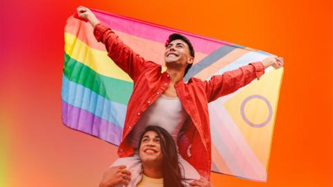 person sitting on another's shoulders holding pride flag. background of orange