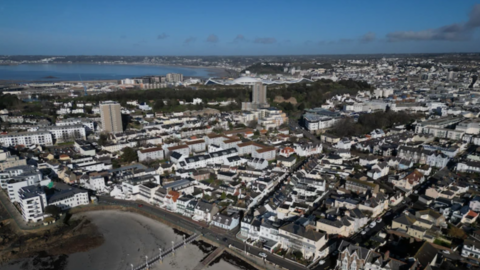A drone shot of Jersey. There is a blue sky, and the sea is in the background.